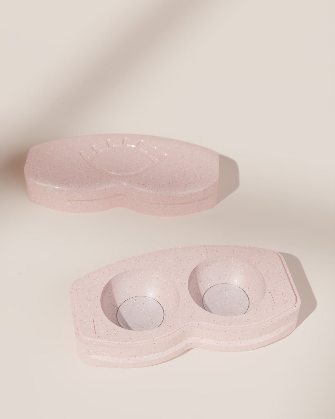 An open pink speckled Lenspod case seen from above, its lid set beside it, a contact lens in each of the two wells.