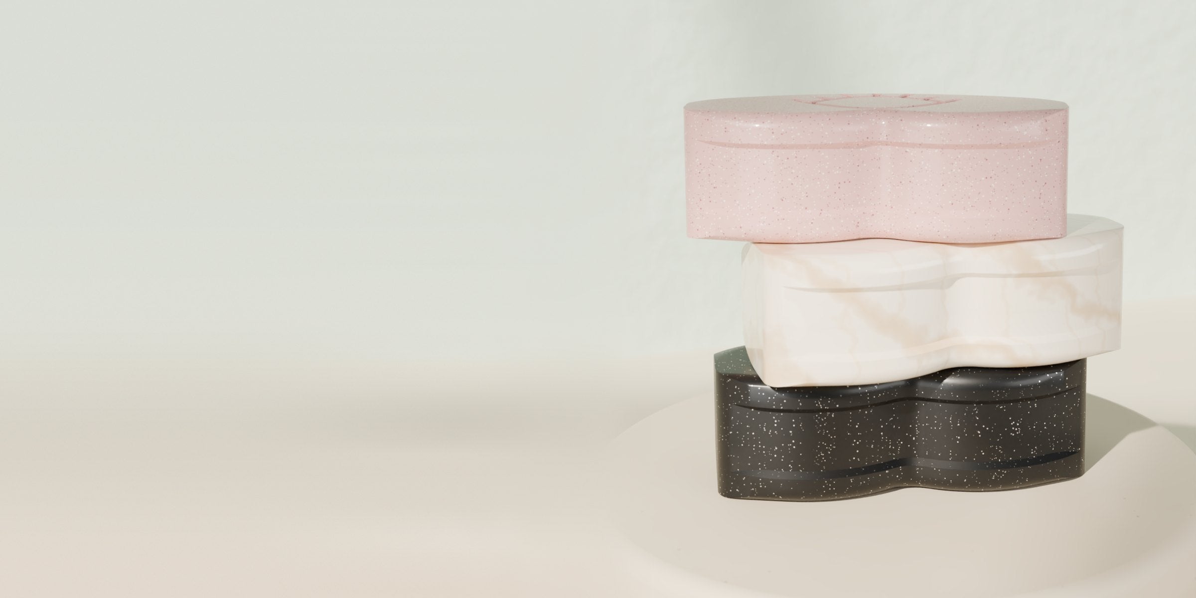 Three Lenspod cases stacked on a stone plinth against a light jade wall: pink speckled on top, cream marble with gold veining in the middle, black sparkle at the bottom.